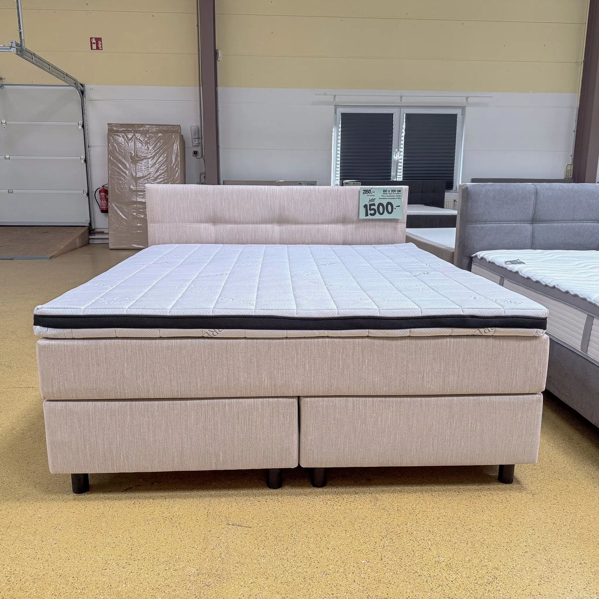 Boxspringbett Theo 180x200 in Beige mit fein gewebtem Stoffbezug, horizontal gestepptem Kopfteil und Visco-Komfortschaumtopper, schräge Vorderansicht